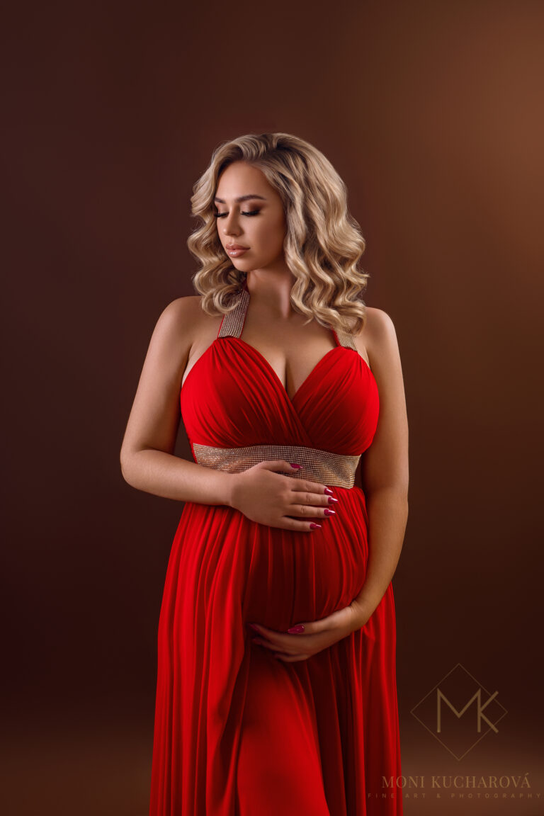 Ukážka luxusného tehotenského fotenia v Bratislave. Krásna tehotná žena v elegantných červených šatách na tmavom pozadí. Profesionálny fine art portrét vytvorený fotografkou Moni Kucharovou.